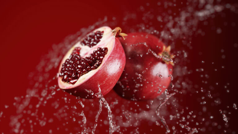 3D product visualization of flying fresh juicy pomegranates in water splashes on a bright red background